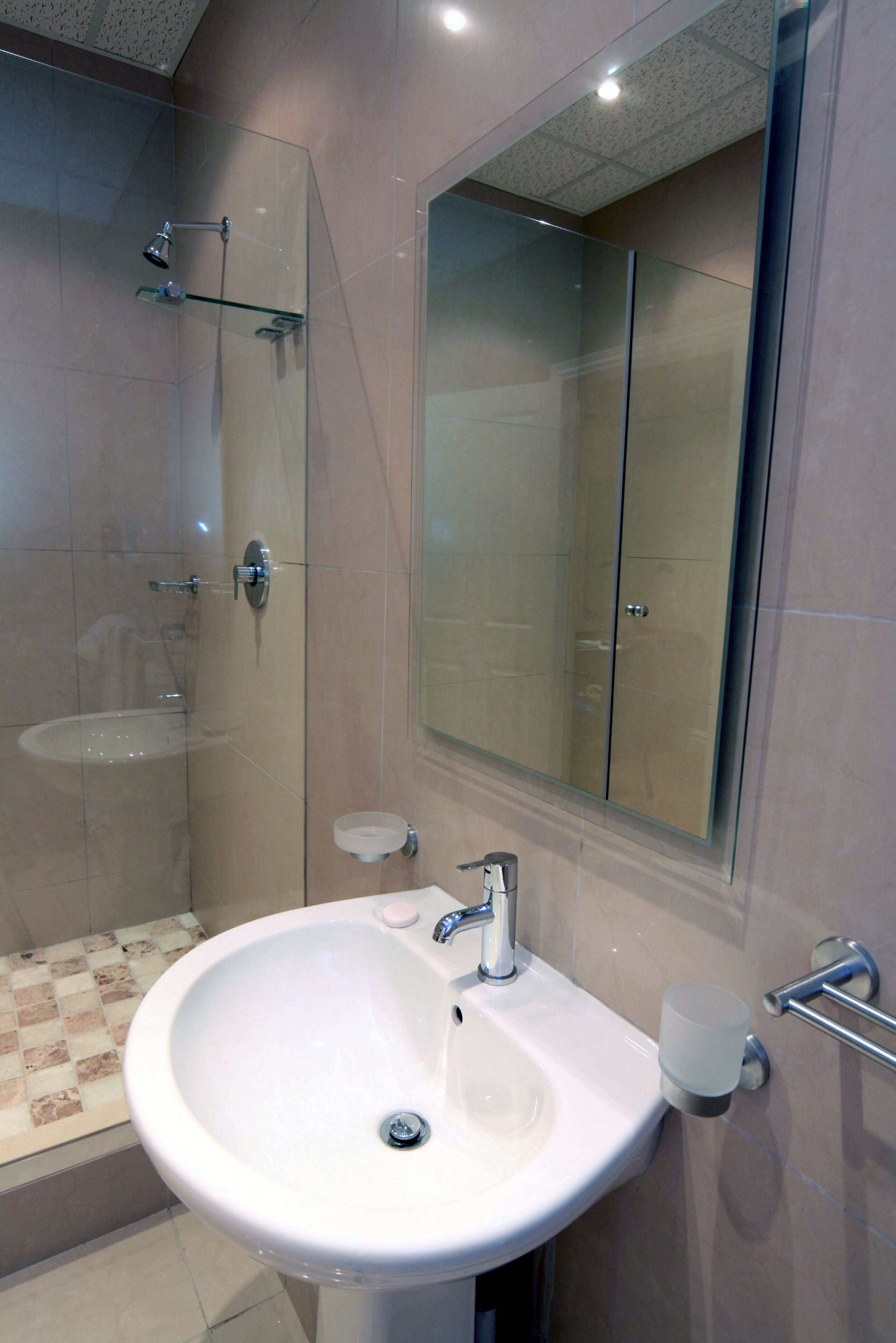 Un baño con cabina de ducha de vidrio, un lavamanos con portavasos y un espejo grande.