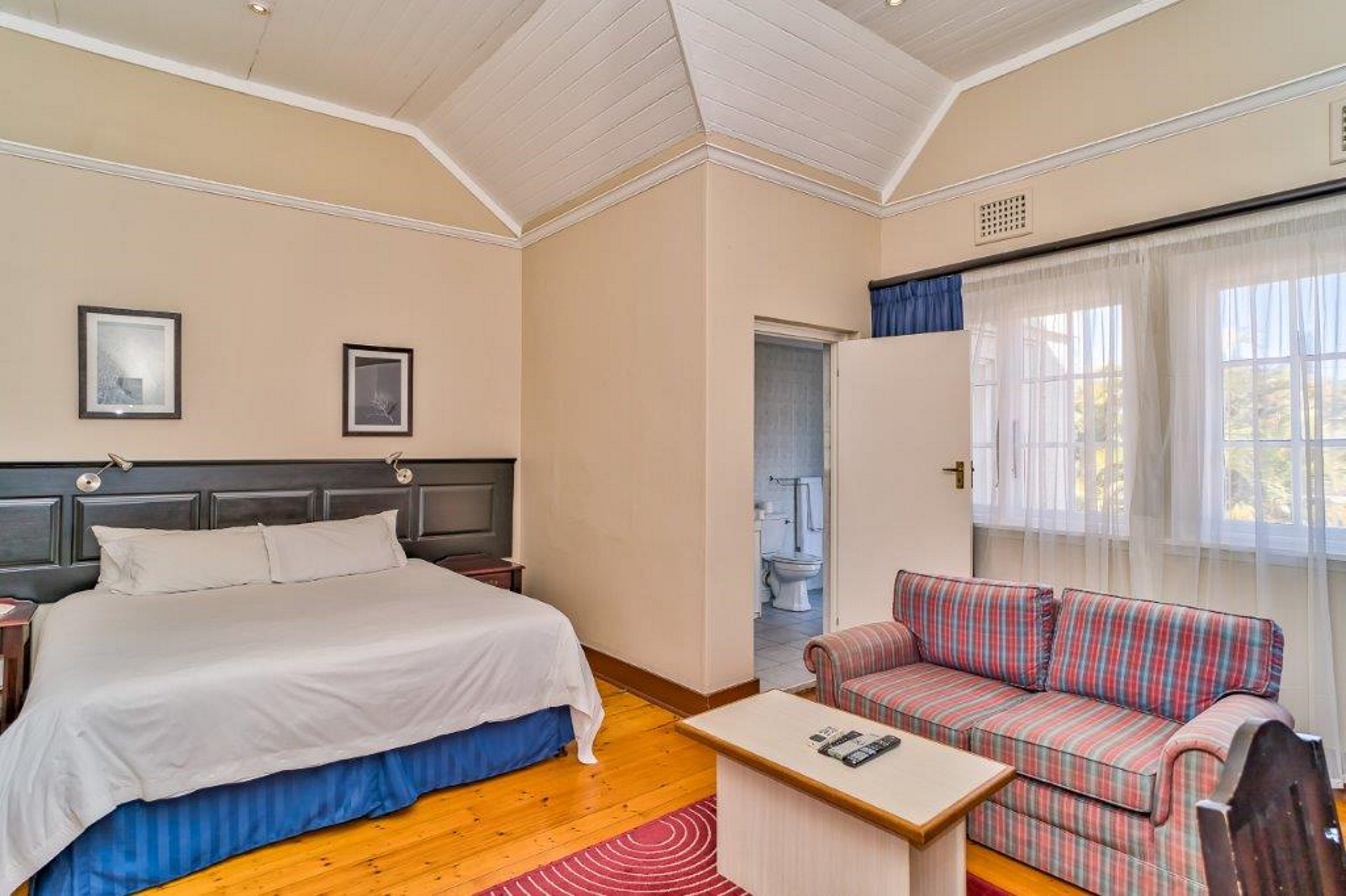 A bedroom with a bed, a sofa, a small table, and a window with curtains.