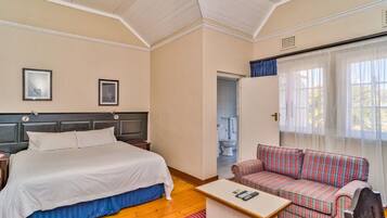 A bedroom with a bed, a sofa, a small table, and a window with curtains.