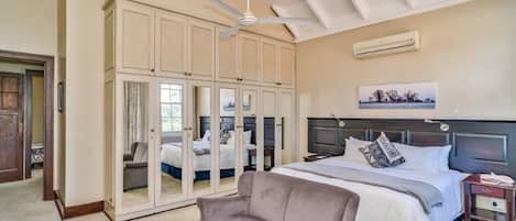 A bedroom with a large bed, a wardrobe, a ceiling fan, and an air conditioning unit.