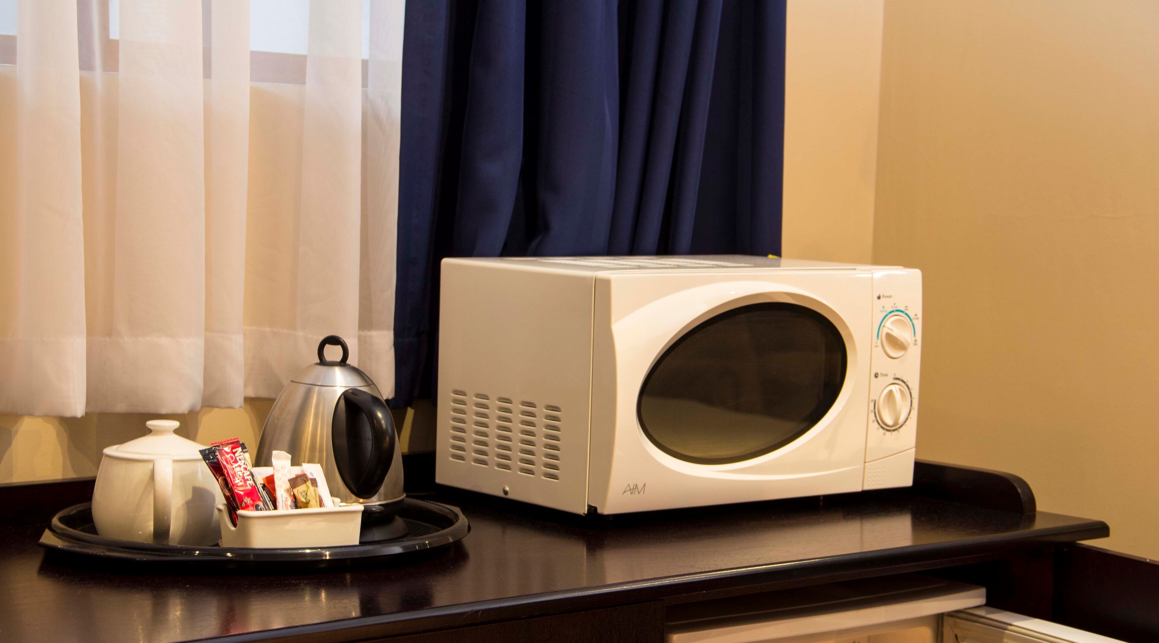 A microwave on a dark countertop with a tea kettle and a tray of snacks.