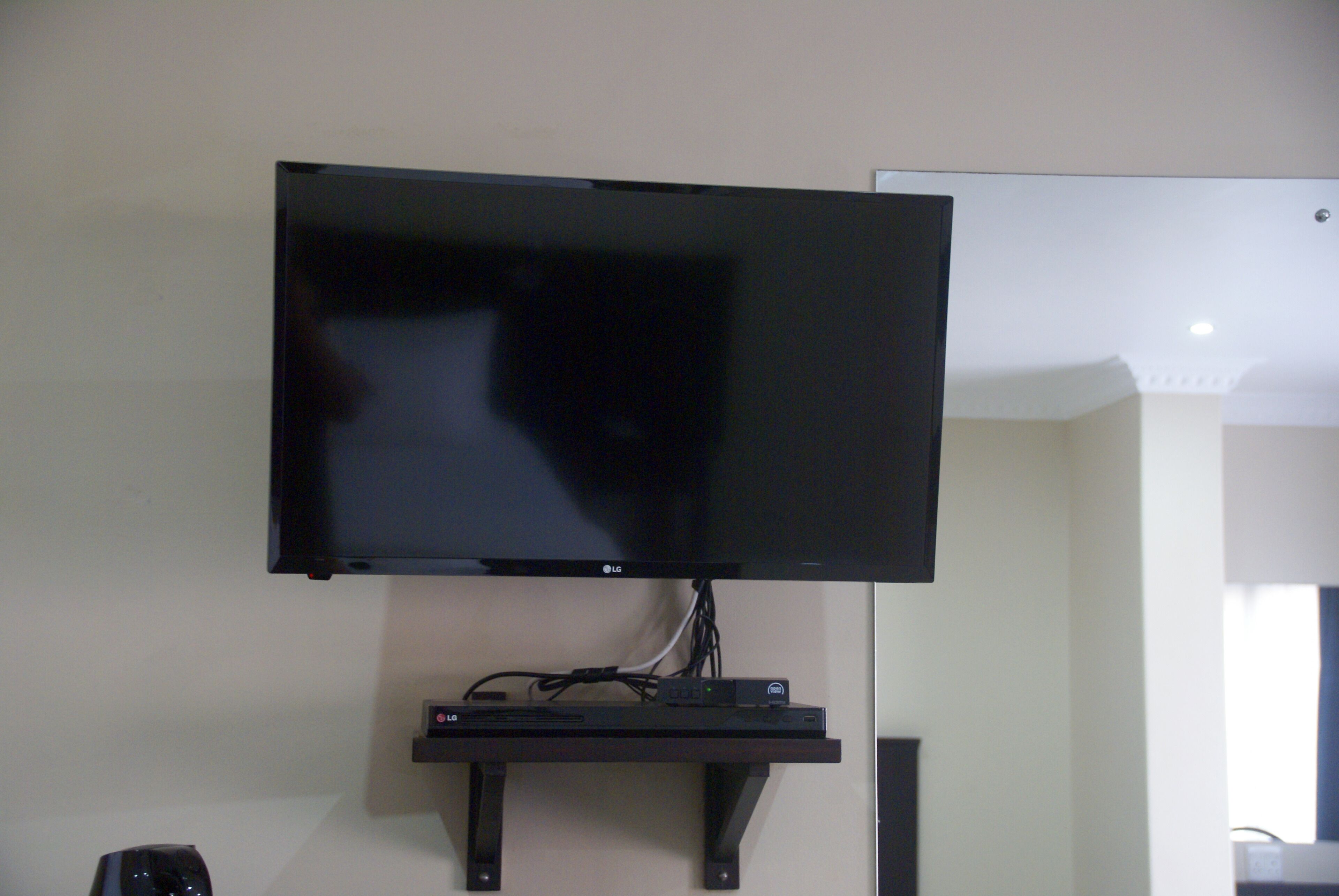 A flat-screen TV mounted on a wall with a shelf below it.