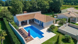 Uma casa com piscina, varanda coberta e vista para o verde ao redor.