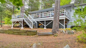 A two-story cabin with a balcony, surrounded by trees and a wooden deck. - Quiet Retreat on Lake w/ Kayaks, Boats + Bikes! (Wautoma)