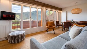 Una sala de estar moderna con un televisor grande, asientos cómodos y vistas a montañas a través de amplios ventanales.