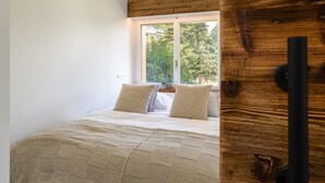 Un dormitorio con un ventanal grande, una cama con ropa de cama estampada y un cabecero de madera.