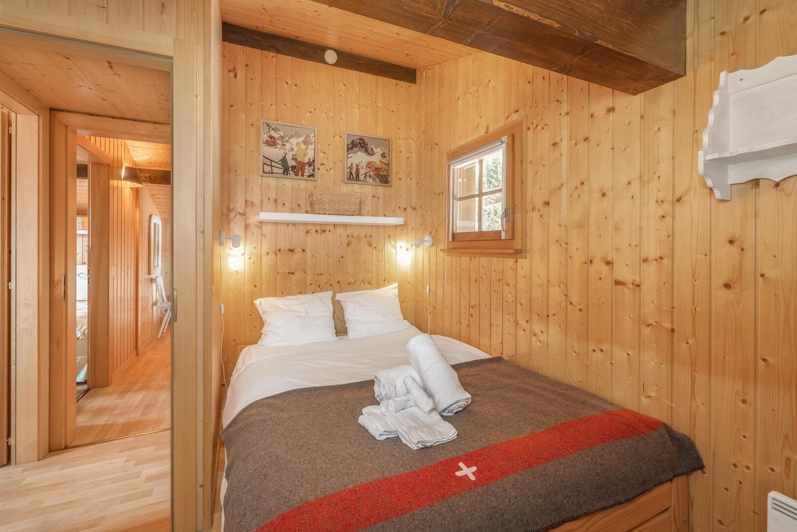 A wooden-paneled room with a bed, a window, and two wall-mounted pictures.