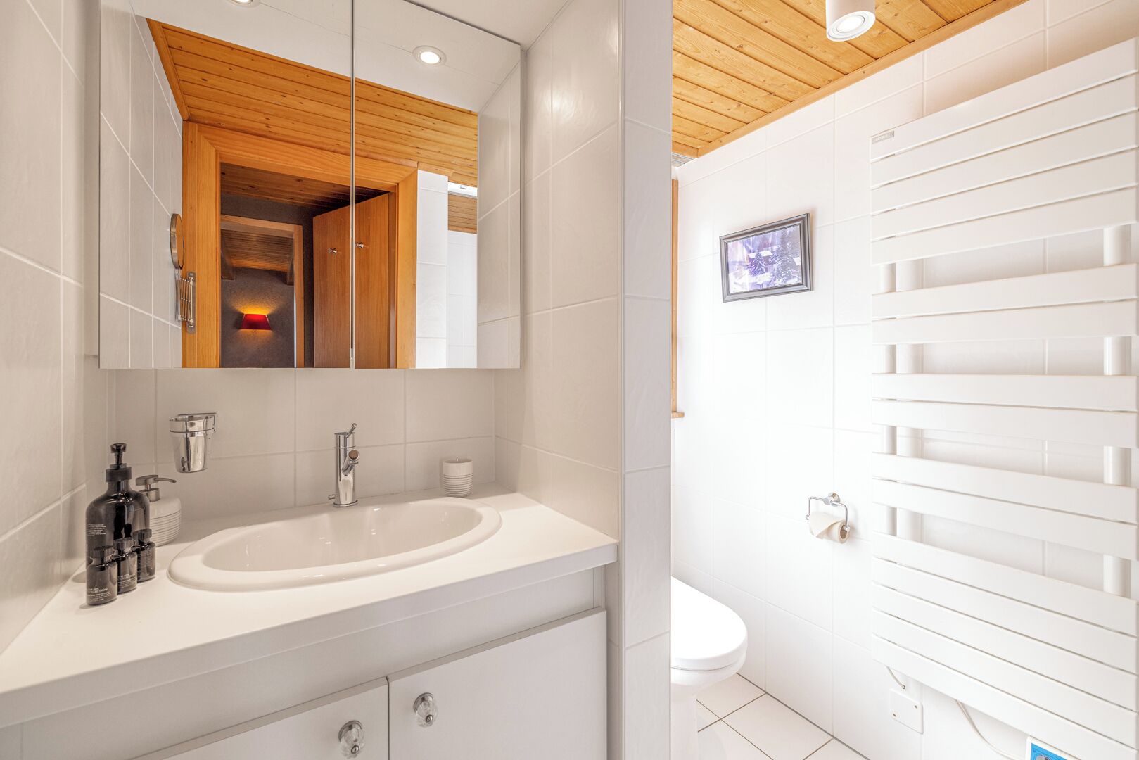 A modern bathroom with a wooden ceiling, a large mirror, a white sink, and a toilet.