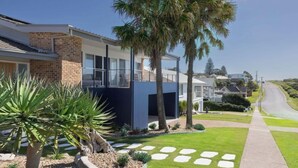 Une maison moderne à deux étages, dotée d’un balcon, d’une pelouse bien entretenue et donnant sur une route dégagée au loin.
