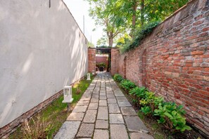 A narrow brick pathway flanked by a white wall and a brick wall with greenery.