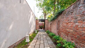 A narrow pathway flanked by a brick wall and a white wall, leading to a covered entrance.