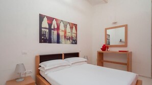 A bedroom with a bed, a nightstand, a bedside table, a mirror, and a wall with a painting.