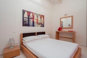 A bedroom with a bed, a nightstand, a bedside table, a mirror, and a wall with a painting.