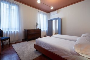 A bedroom with two beds, a dresser, a chair, and a window with curtains.