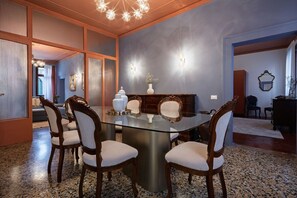 A modern dining area with a glass table surrounded by chairs, a decorative vase, and wall sconces.
