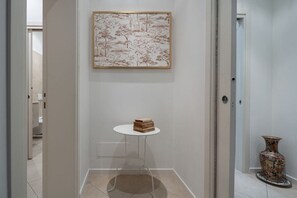 A hallway with a framed artwork on the wall, a small table with books, and a decorative vase.