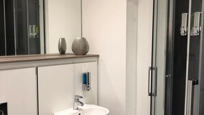 Un baño moderno con lavamanos blanco, cabina de ducha con mampara de vidrio y espejo sobre el lavamanos.