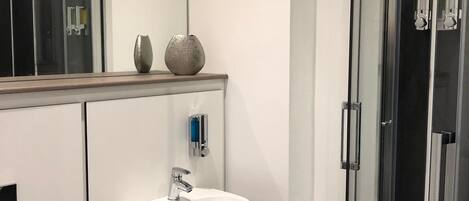 Een moderne badkamer met een wit wastafelmeubel, een douchecabine van glas en een spiegel boven het wastafelmeubel.