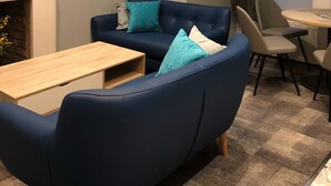 Una sala de estar moderna con un sofá azul, una mesa de centro de madera y una mesa de comedor con sillas.