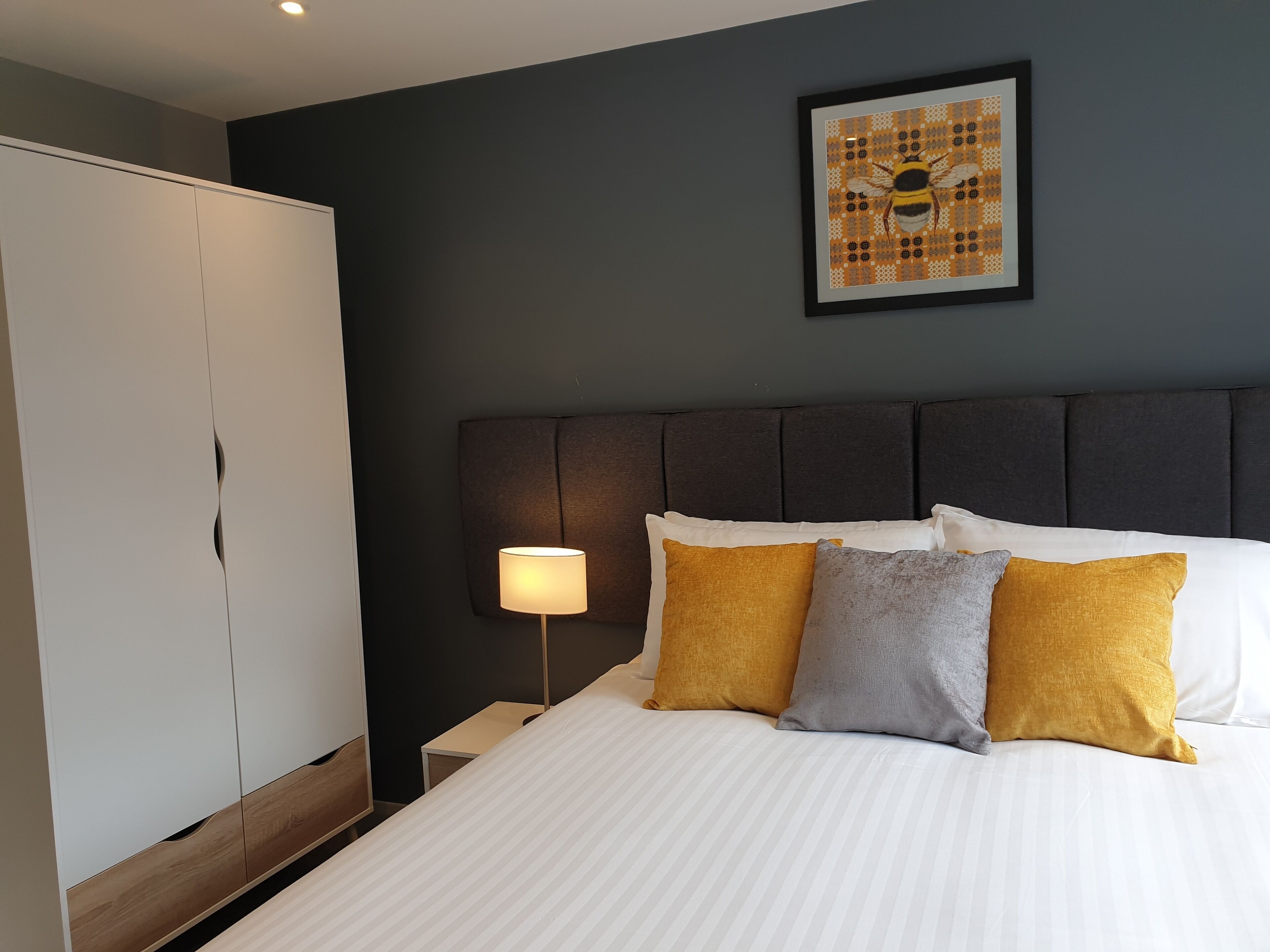 A hotel room with a bed, a nightstand, a lamp, a wardrobe, and a framed artwork on the wall.