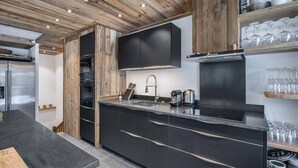 A modern kitchen with wooden ceiling beams, black cabinetry, and a central island with a sink.