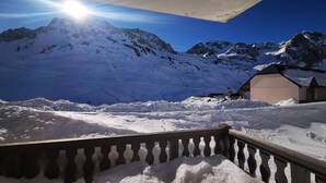 A snow-covered mountain landscape with a building and a wooden railing in the foreground. - Charming apartment with parking - 6 guests (La Mongie)