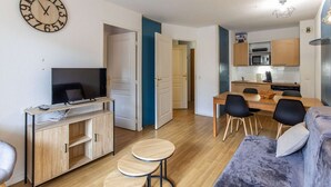 A compact living space with a TV, wooden cabinet, sofa, dining table, chairs, and a kitchen area. - Charming apartment with parking - 6 guests (La Mongie)