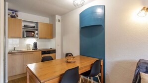 A compact kitchen with wooden cabinets, a microwave, and a dining table with chairs. - Charming apartment with parking - 6 guests (La Mongie)