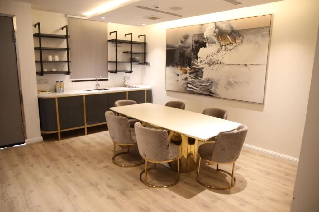 A modern kitchen with a dining area, featuring a long table with six chairs, a large abstract painting, and built-in shelves.