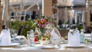 Una mesa dispuesta para una comida, con un centro de mesa floral, copas de cristal transparente y diferentes platos.