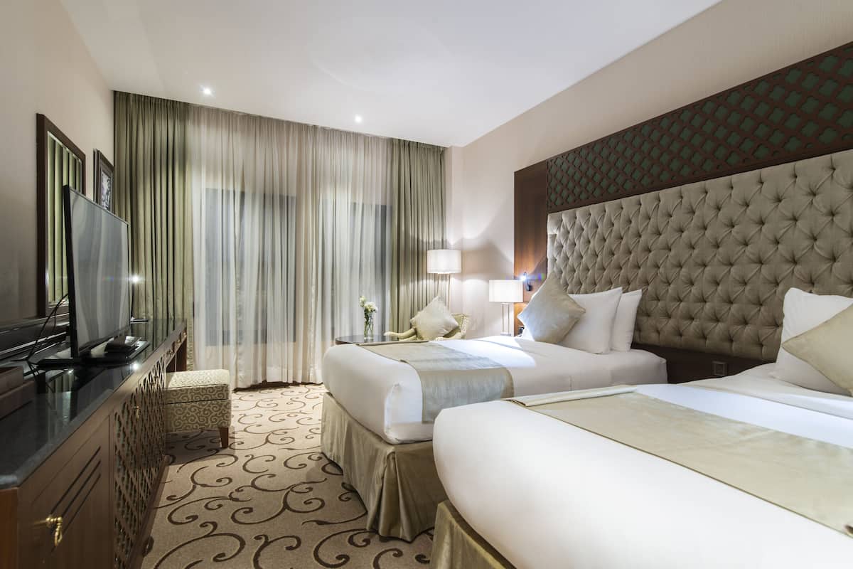 Ein Hotelzimmer mit zwei Betten, einem Fernseher, einem Schreibtisch und einem großen Fenster mit Vorhängen.