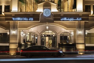 El exterior del Palacio Vittori con señalización iluminada y un coche negro estacionado al frente.