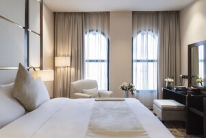 Una habitación de hotel con una cama grande, una silla, un escritorio y dos ventanas con cortinas.