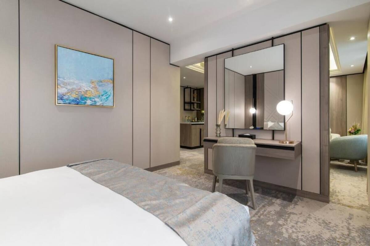 Ein Hotelzimmer mit einem Bett, einem Schreibtisch mit Spiegel, einem Sessel und einem Bild an der Wand.