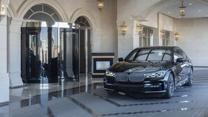 Un BMW negro estacionado en un vestíbulo de diseño moderno, que cuenta con un ascensor de vidrio y elegantes lámparas.