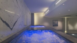 Un área de spa con dos jacuzzis, paredes de mármol y un diseño de techo moderno.