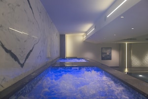 A spa area with two hot tubs, marble walls, and a modern ceiling design.