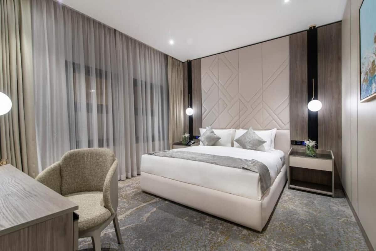 Ein modernes Hotelzimmer mit einem großen Bett, einem Schreibtisch, einem Stuhl und einem Nachttisch.