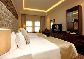A hotel room with two beds, a television, a desk with a computer, and a large mirror.