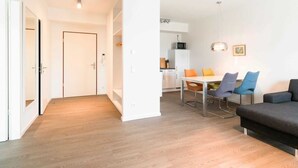 Eine moderne Wohnung mit Holzboden, einem Essbereich mit Tisch und Stühlen, einer Couch und einer Küche im Hintergrund.