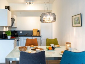 A modern kitchen with white cabinets, a dining table with chairs, and a chandelier. - Hafenspitze App. 04, Deutschland (Wismar)