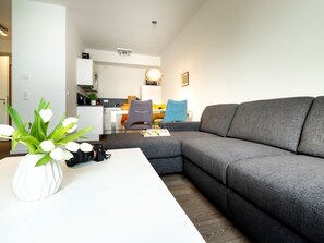 A modern living room with a grey sectional sofa, a white coffee table, and a vase with white flowers. - Hafenspitze App. 04, Deutschland (Wismar)