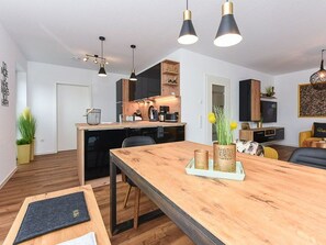 A modern kitchen with wooden cabinets, a dining table with chairs, and pendant lighting. - Deichkinder Carolinensiel (Wittmund)