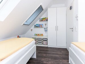 A room with a sloped ceiling, a skylight, two beds, a wardrobe, a desk with storage, and educational wall decorations. - Deichkinder Carolinensiel (Wittmund)