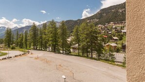 A parking area with a snow-covered mountain in the background, surrounded by trees and a small village.