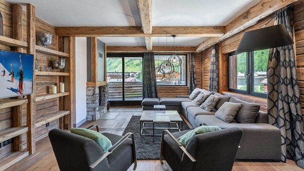 A cozy log cabin interior with a stone fireplace, a sofa, and a television displaying a ski scene. - Luxury 8-Person Apartment with Sauna, Parking, and Balcony in Central Val d'Isère (Val-d'Isère)