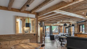 A rustic interior with exposed wooden beams, a round wooden table with chairs, and a sofa in a spacious room with large windows. - Luxury 8-Person Apartment with Sauna, Parking, and Balcony in Central Val d'Isère (Val-d'Isère)