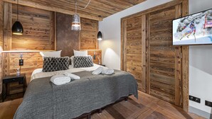 A bedroom with a wooden ceiling, a bed with a grey blanket, two pillows, a TV on the wall, and a wooden wardrobe. - Luxury 8-Person Apartment with Sauna, Parking, and Balcony in Central Val d'Isère (Val-d'Isère)