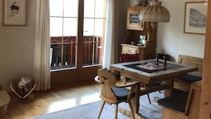 A wooden dining area with a table and chairs, a hanging light fixture, and a large window with curtains.