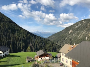 Un pueblo de montaña con casas tradicionales, un campo verde y un valle boscoso.